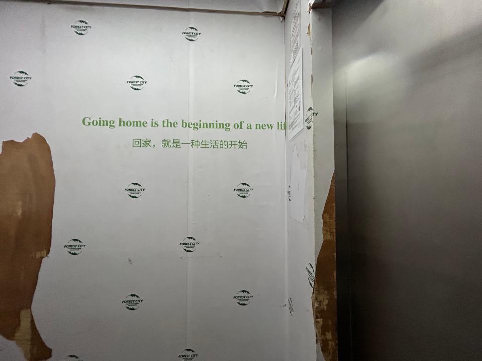 An elevator with torn wallpaper inside that reads, "Going home is the beginning of a new life."
