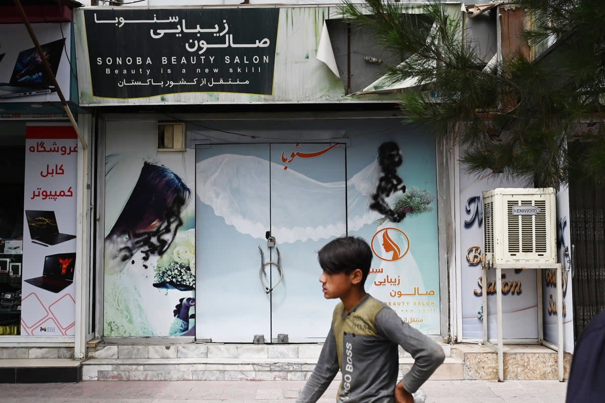 A youth walks past a closed beauty salon with images of women defaced at Shahr-e Naw area in Kabul (AFP via Getty Images)