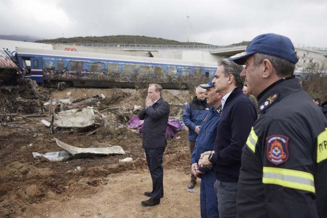 In this photo provided by the Greek Prime Minister's Office, Greece's Prime Minister Kyriakos Mitsotakis, second right, accompanied by Transport Minister Kostas Karamanlis, left, holding his face, looks the debris of trains after a collision in Tempe, about 376 kilometres (235 miles) north of Athens, near Larissa city, Greece, Wednesday, March 1, 2023. A passenger train carrying hundreds of people, including many university students returning home from holiday, has collided at high speed with an oncoming freight train. (Dimitris Papamitsos/Greek Prime Minister's Office via AP)