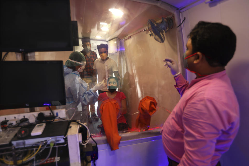 A woman looks at health workers as she gets ready to give nasal swab sample for COVID- 19 testing through rapid antigen methodology inside a mobile lab in New Delhi, India, Monday, Aug. 10, 2020. India is the third hardest-hit country by the pandemic in the world after the United States and Brazil. (AP Photo/Manish Swarup)