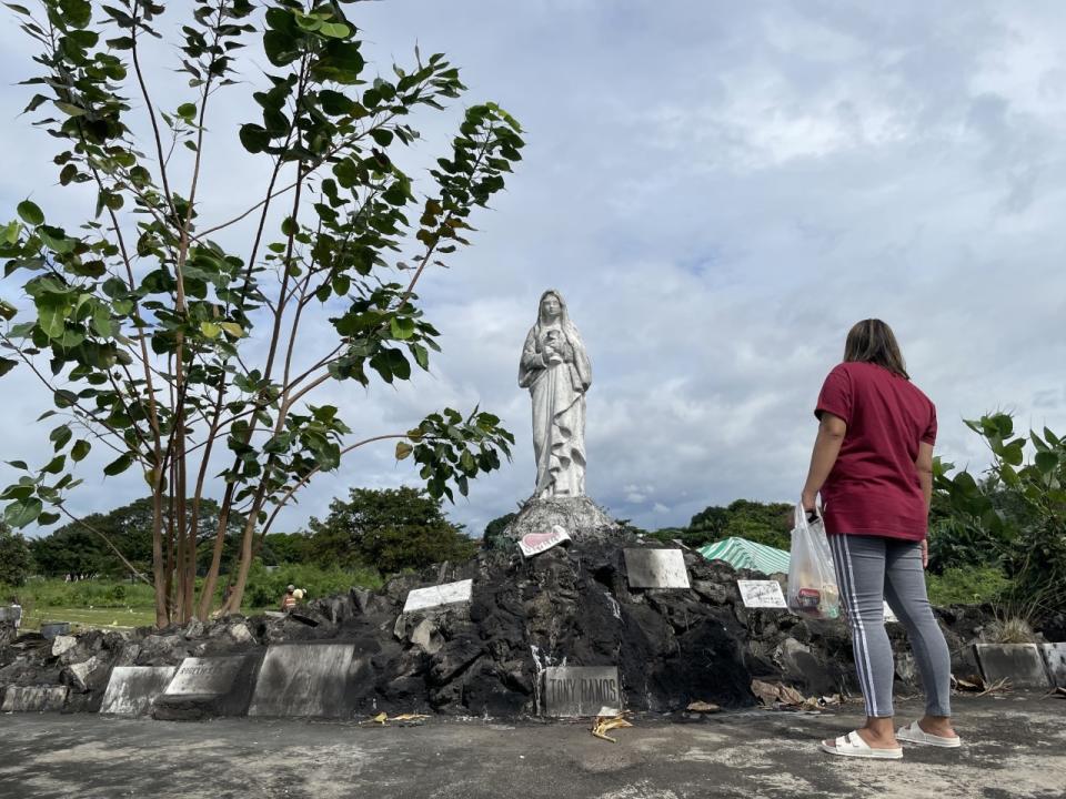 A woman stands in front of a statue at a cemetery