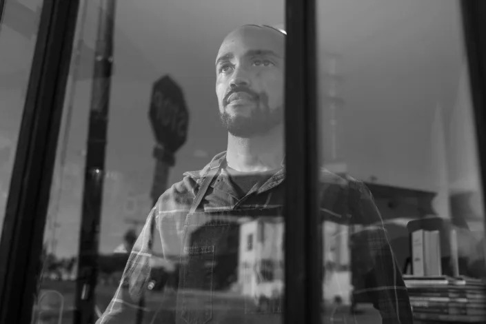 Jeff Rambo, seen through a window, stands in his coffee shop, Storymakers Coffee Roasters.