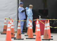 Healthcare workers help each other with their personal protective equipment at a drive-through coronavirus testing site, Sunday, July 5, 2020, outside Hard Rock Stadium in Miami Gardens, Fla. Florida health officials say the state has reached a grim milestone: more than 200,000 people have tested positive for the novel coronavirus since the start of the outbreak. (AP Photo/Wilfredo Lee)