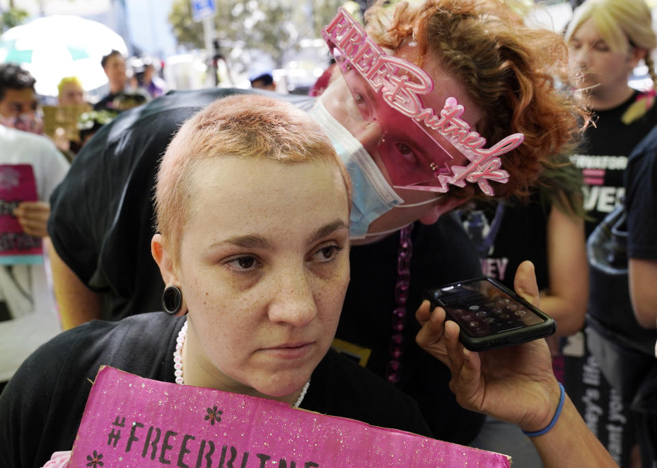 Britney Spears supporters Jennifer Preston, left, and Jakeyonce listen to a feed from court on a cellphone, outside a hearing concerning the pop singer's conservatorship at the Stanley Mosk Courthouse, Wednesday, June 23, 2021, in Los Angeles. (AP Photo/Chris Pizzello)