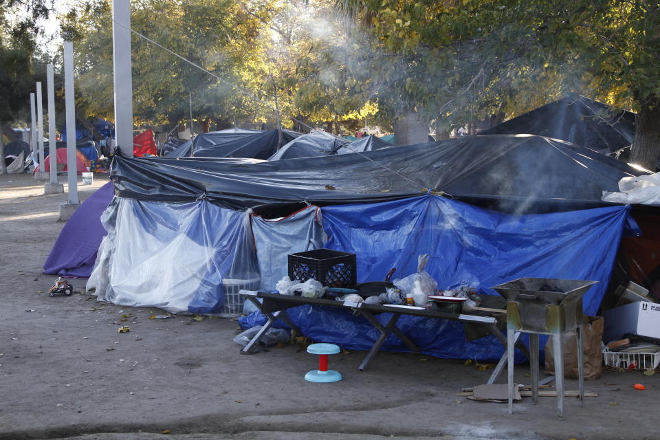 In this Tuesday, Dec. 3, 2019 photo, smoke rises from a wood fire stove at a tent encampment in a public park in Juarez, Mexico, a quarter of a mile away from a border crossing to El Paso, Texas. Residents of the camp said that they are fleeing violence and gang impunity in southern Mexico. Those at the front of the line say they've been in the camp for 10 weeks. (AP Photo/Cedar Attanasio)