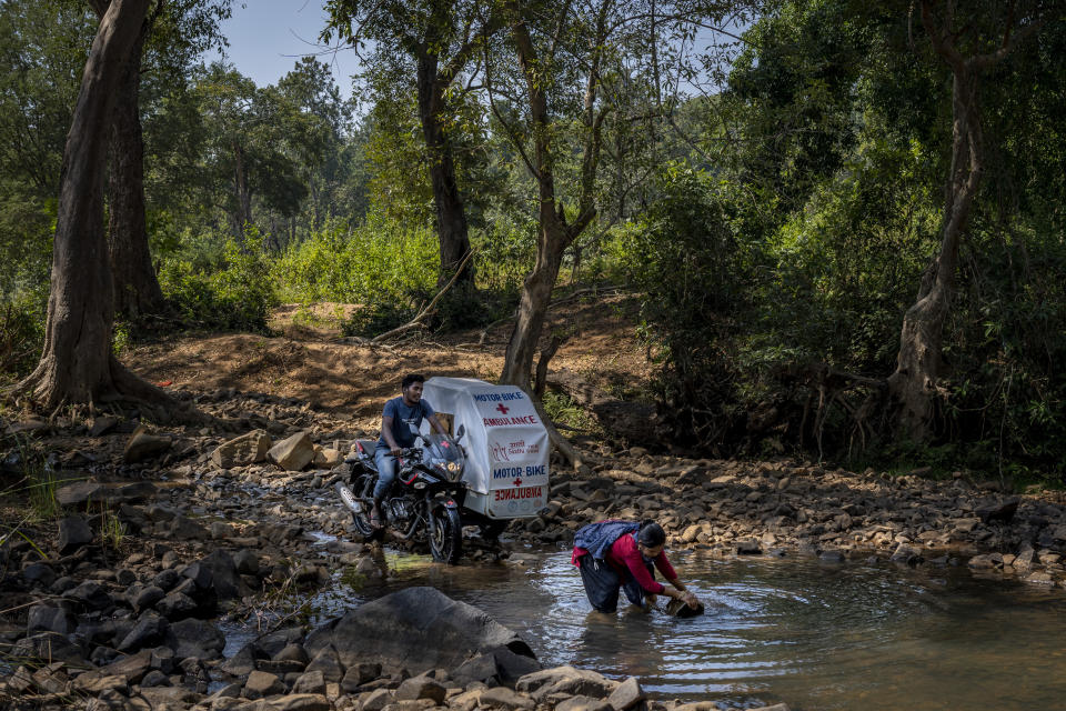 Lata Netam, a health worker, tries to remove a boulder as Sukhram Vadde, 24, awaits on a motorbike ambulance, a two-wheeler with a sidecar consisting of a hospital bed on wheels, to cross a stream through Abhujmarh, or "the unknown hills," to reach a pregnant woman in Kodoli, a remote village near Orchha in central India's Chhattisgarh state, Nov. 15, 2022. These ambulances, first deployed in 2014, reach inaccessible villages to bring pregnant women to an early referral center, a building close to the hospital where expectant mothers can stay under observation, routinely visit doctors if needed until they give birth. Since then the number of babies born in hospitals has doubled to a yearly average of about 162 births each year, from just 76 in 2014. The state has one of the highest rates of pregnancy-related deaths for mothers in India, about 1.5 times the national average, with 137 pregnancy related deaths for mothers per 100,000 births. (AP Photo/Altaf Qadri)