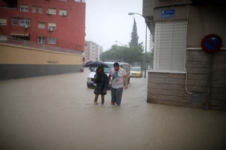 People cross a flooded street close to the overflowing Segura river as torrential rains hit Orihuela