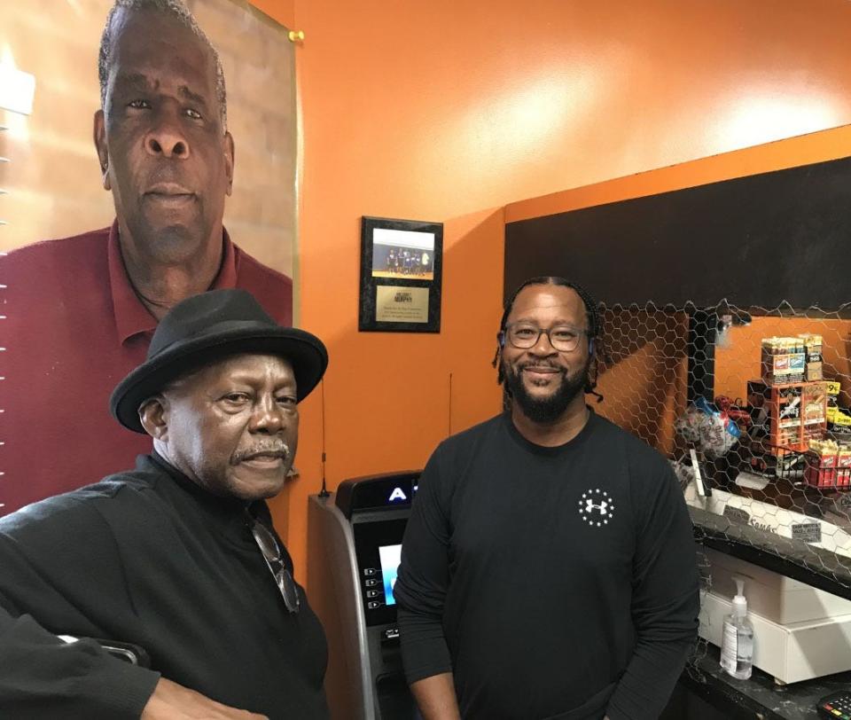 Fred Taylor (left) and Will Bordeaux in front of a picture of the late William Murphy at Bordeaux's 1 Stop Shop and Grocery in Wilmington. Taylor and Bordeaux played in and attended the once-annual Turkey Bowl football game, and Murphy, who died in 2009, helped organize it.