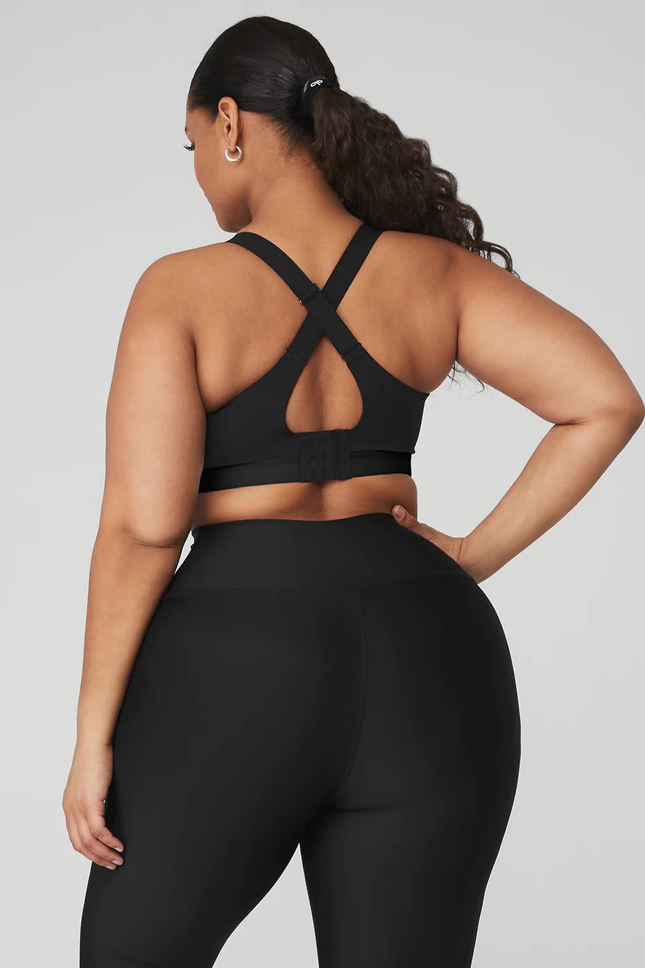 a model wearing a black sports bra by alo in front of a plain backdrop in a roundup of the best sports bras for women 2023