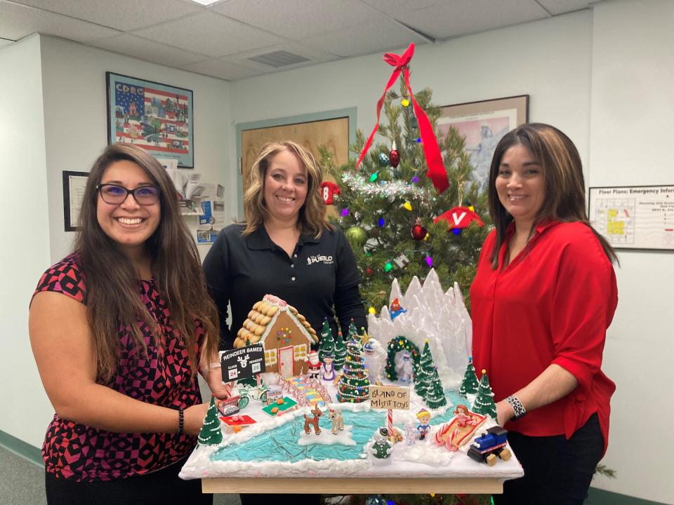 From left: Lexi Romero Stewart, Beth Mauro and Venessa Codina hold up their department's gingerbread house display, inspired by the 1964 film "Rudolph the Red-Nosed Reindeer," at the Pueblo Department of Housing and Citizen Services office on Dec. 20, 2023.