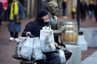 A man poses for a photograph with his shopping bags and a statue of hall of fame Boston Celtics coach Red Auerbach on Black Friday in Boston, Massachusetts November 29, 2013. Black Friday, the day following the Thanksgiving Day holiday, has traditionally been the busiest shopping day in the United States. REUTERS/Brian Snyder