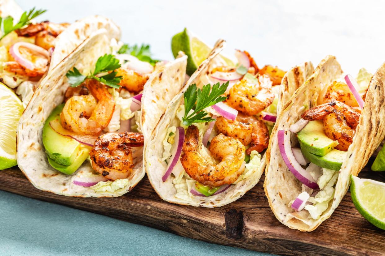 Shrimp tacos. Seafood fajitas with cabbage, onion, parsley in tortillas served on wooden cutting board