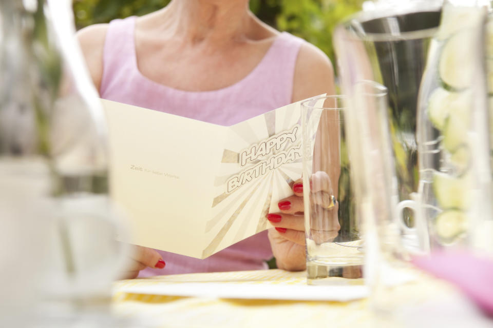 A woman reading a birthday card at a table set for a celebration, holding a glass with a pitcher of water and other items visible