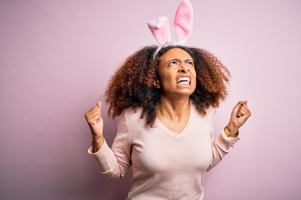 Young african american woman with afro hair wearing bunny ears over pink background crazy and mad shouting and yelling with aggressive expression and arms raised. Frustration concept.