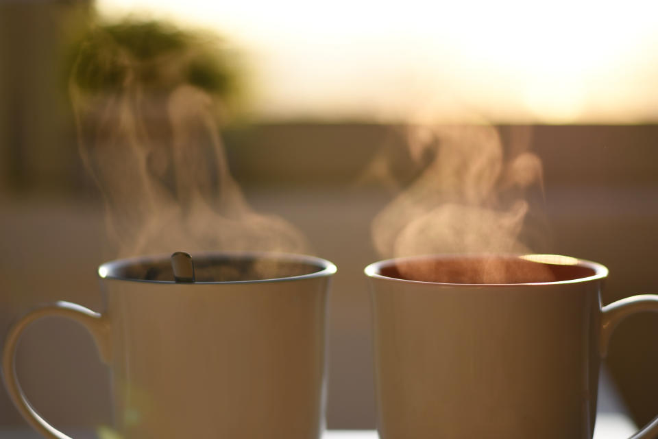 two steaming mugs of coffee on an outdoor table.