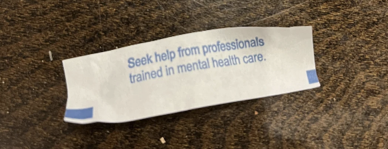 Fortune cookie message on wooden table reads: "Seek help from professionals trained in mental health care."