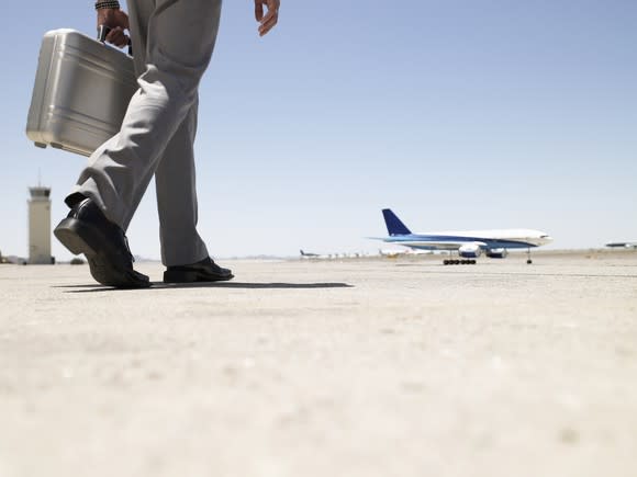 Man in grey suit pants and black shoes holding a briefcase and walking to an airplane