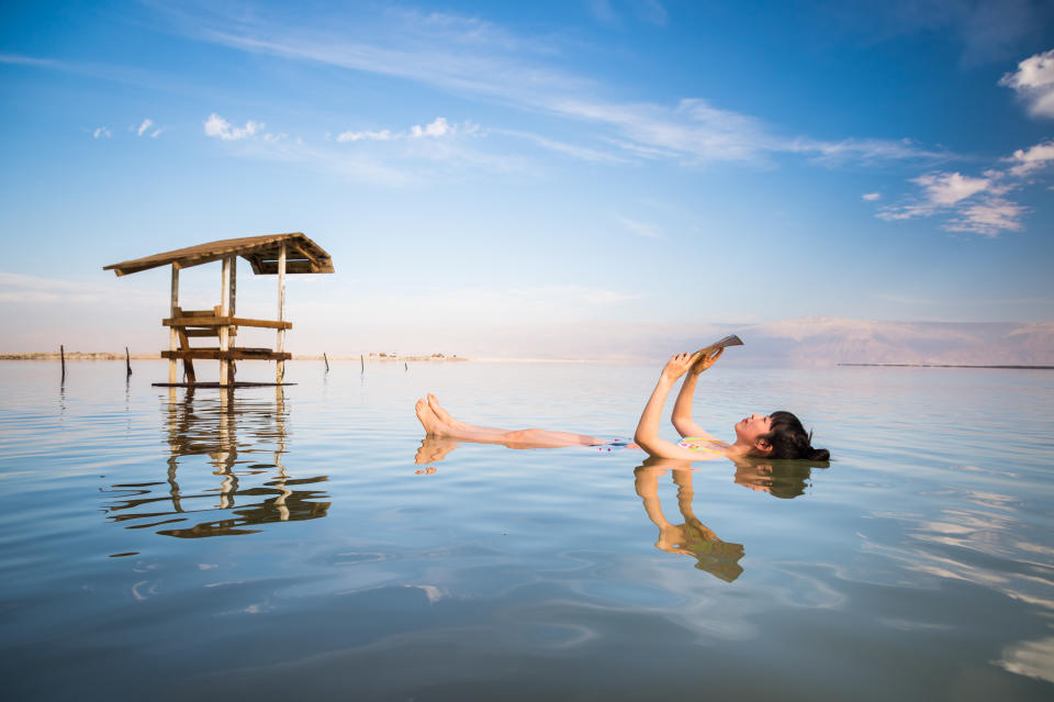 A woman floats along the Dead Sea facing up, and reads a magazine as she floats.