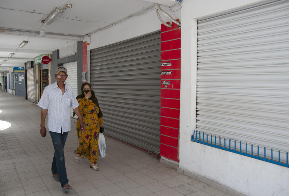 People walk past closed shops in La Marsa district,just outside Tunis, Monday, May, 10, 2021. Tunisia announced on Friday strict new measures to try to contain the spread of the coronavirus, with the prime minister saying that the health system risks collapsing if something is not done. Houses of prayer are being ordered closed starting Sunday for a week, along with outdoor markets and large stores and malls. Shops selling food can remain open. (AP Photo/Hassene Dridi)