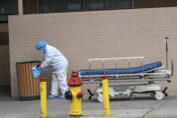 Medical personnel remove their personal protective equipment after delivering a bodies from the Wyckoff Heights Medical Center to refrigerated containers parked outside, Thursday, April 2, 2020 in the Brooklyn borough of New York. As coronavirus hot spots and death tolls flared around the U.S., the nation's biggest city was the hardest hit of the all, with bodies loaded onto refrigerated morgue trucks by gurney and forklift outside overwhelmed hospitals, in full view of passing motorists. (AP Photo/Mary Altaffer)