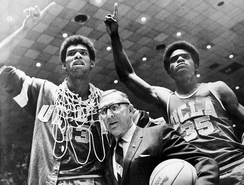 FILE - UCLA coach John Wooden is flanked by Sidney Wicks, right, and Lew Alcindor, draped with basket ropes, after the UCLA team beat Purdue 92-72 to win the NCAA basketball title for the third consecutive year, in Louisville, Ky., March 24, 1969. (AP Photo/File)