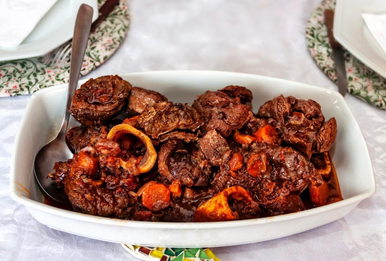 veal, onion, and carrot in a dark sauce in white tray