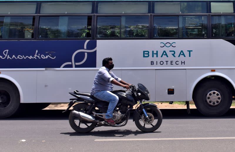 FILE PHOTO: A man rides his motorcycle past a parked bus of Indian biotechnology company Bharat Biotech outside its office in Hyderabad
