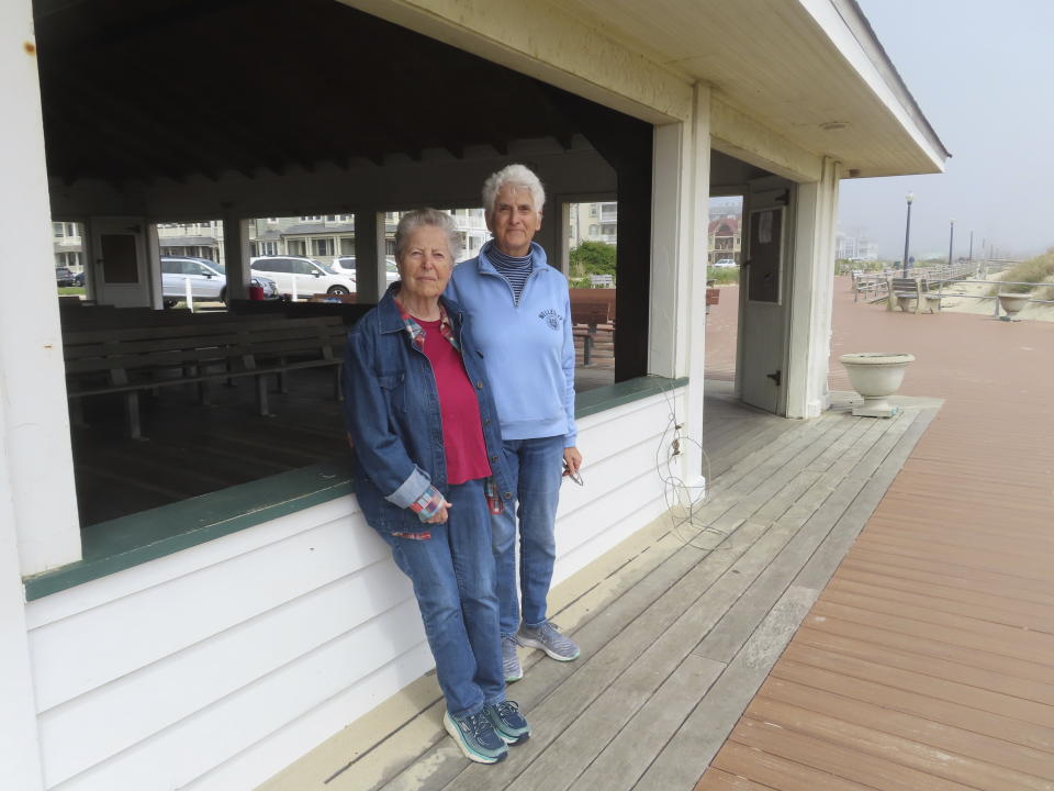 Luisa Paster, left, and Harriet Bernstein, right pose on the boardwalk in Ocean Grove, N.J. on May 2, 2024, near a pavilion where a religious group that owns all the land in Ocean Grove refused to let them hold a civil union ceremony in 2007. The state of New Jersey says the Ocean Grove Camp Meeting Association is violating state beach access laws by keeping people off the beach until noon on Sundays. (AP Photo/Wayne Parry)