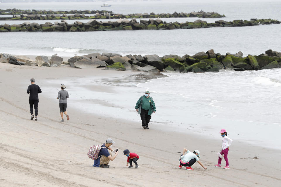 Children play in the sand while others jog as a New York City Parks officer, center, walks the beach making sure no one goes in the water, at Coney Island Beach during the current coronavirus outbreak, Sunday, May 24, 2020, in New York. Swimming is prohibited at New York City beaches. (AP Photo/Kathy Willens)