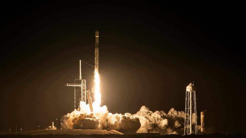 A rocket takes off from the launch pad above a bright cloud of fire and smoke at night