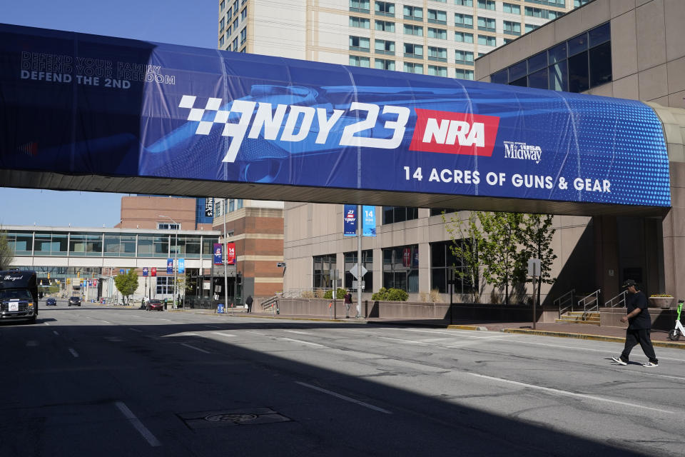 A pedestrian walks under a sign advertising the NRA Convention, Thursday, April 13, 2023, in Indianapolis. The convention starts Friday, April 14 and end on Sunday, April 16. (AP Photo/Darron Cummings)