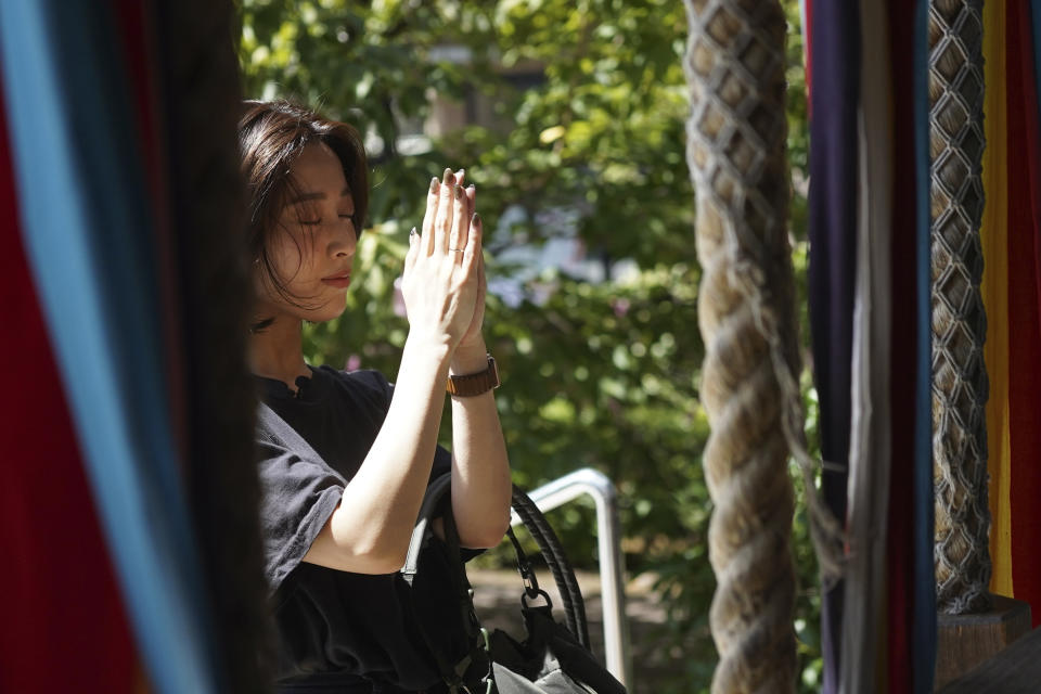 Momo Nomura, a graphic artist and entrepreneur, prays before collecting Goshuin, a seal stamp certifying her visit that comes with elegant calligraphy and the season's drawings, at Sakura Jingu in Tokyo on Aug. 30, 2023. She performs the prescribed rituals - ringing a bell, bowing and clapping. But her main purpose is getting a Goshuin, a stamp with elegant calligraphy that shrines provide for a fee to certify the visit. (AP Photo/Eugene Hoshiko)