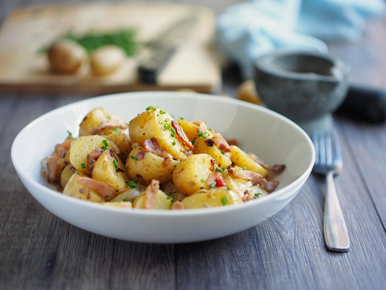 Warm potato salad with bacon and onion in a white bowl and a fork with a blurred background