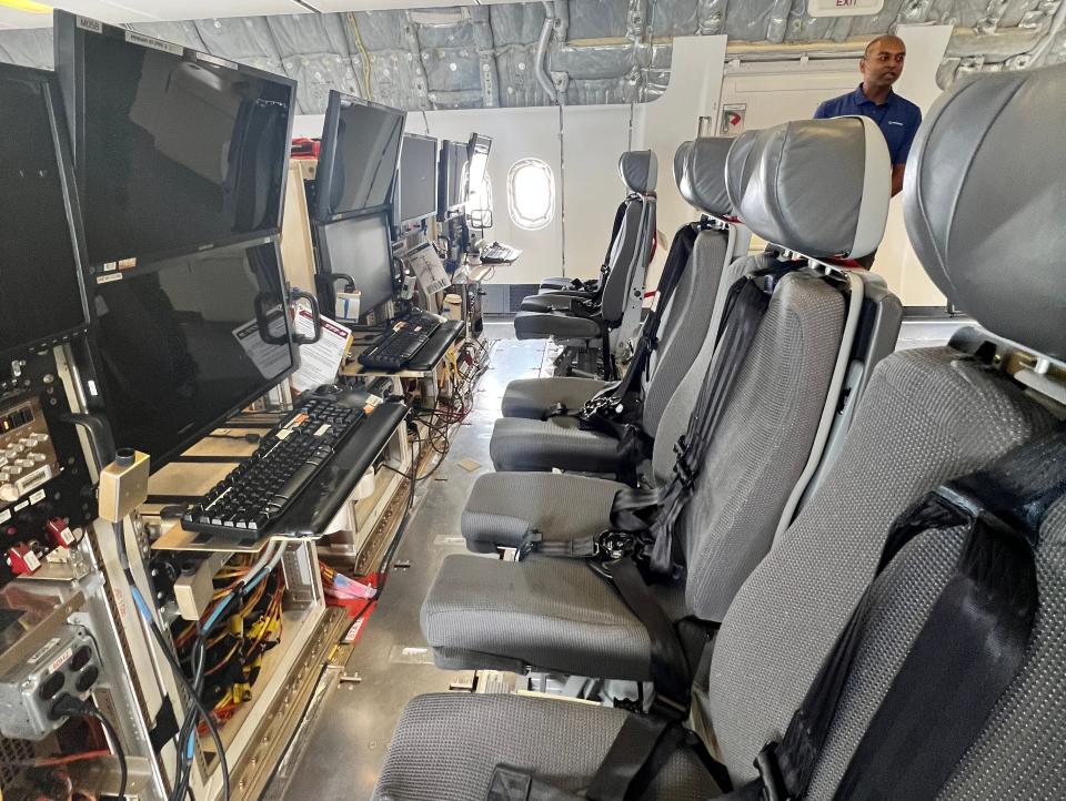 A row of four computer stations each with two monitors and grey seats with overshoulder seatbelts, on board a Boeing 777-9 testbed