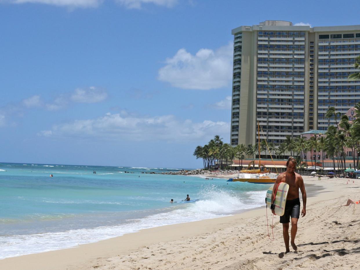 A surfer walks on a sparsely populated Waikiki Beach in Honolulu. A new study has found that O'ahu island could lose 40 per cent of beaches by 2050 (AP)