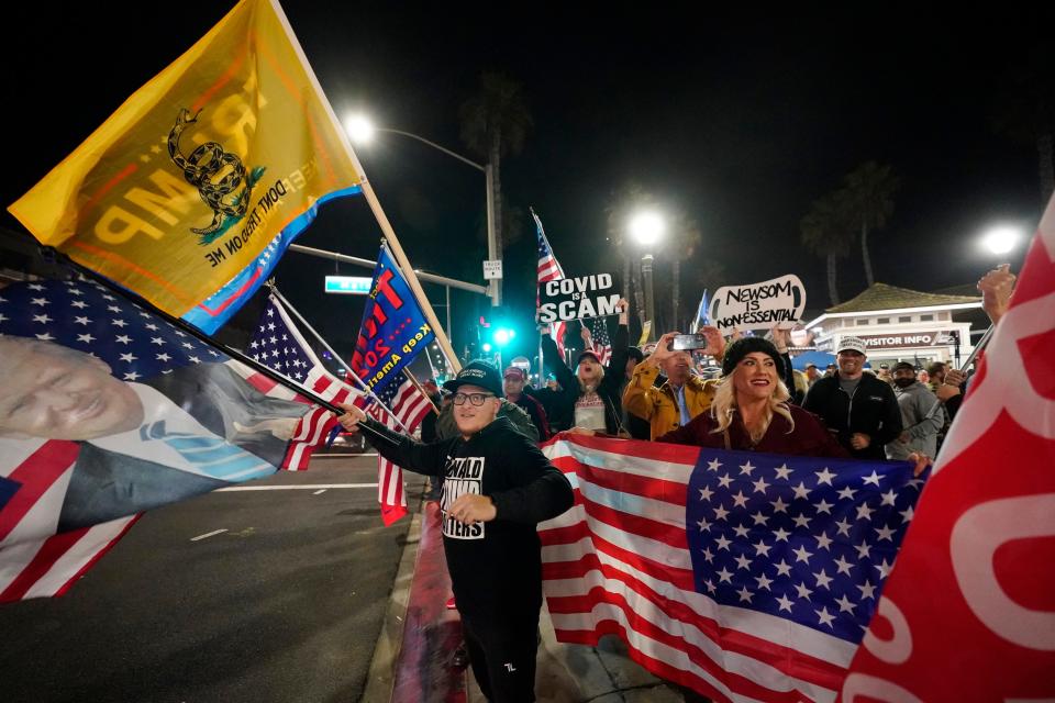 Demonstrators wave flags along Pacific Coast Highway Saturday, Nov. 21, 2020 during a protest against a stay-at-home order amid the COVID-19 pandemic in Huntington Beach, Calif. California health officials are restricting overnight activities starting Saturday night, though there are plenty of exceptions. They're calling it a limited stay-at-home order designed to stem the rapidly spreading coronavirus by discouraging social gatherings.