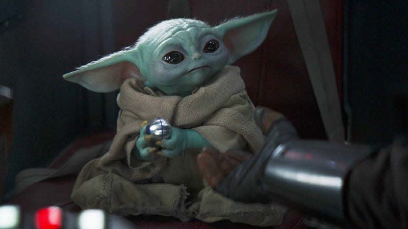 Baby Yoda aka Grogu holds onto a silver ball while sitting in a spaceship. 