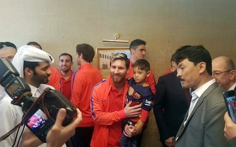 Barcelona's Argentinian forward Lionel Messi (C-L) holding six-year-old Afghan boy Murtaza Ahmadi (C-R) in Doha, upon the team's arrival to play a friendly match against Saudi Arabian side Al-Ahli. - Credit: AFP