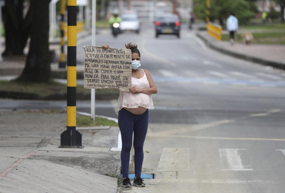 Venezuelan migrant Veronica Hernandez, 20, who is eight months pregnant, holds up a sign with a handwritten message asking for food or money, at a crosswalk in Bogota, Colombia, Tuesday, Feb. 9, 2021. Colombia said Monday it will register hundreds of thousands of Venezuelan migrants and refugees currently in the country without papers, in a bid to provide them with legal residence permits and facilitate their access to health care and legal employment opportunities. (AP Photo/Fernando Vergara)