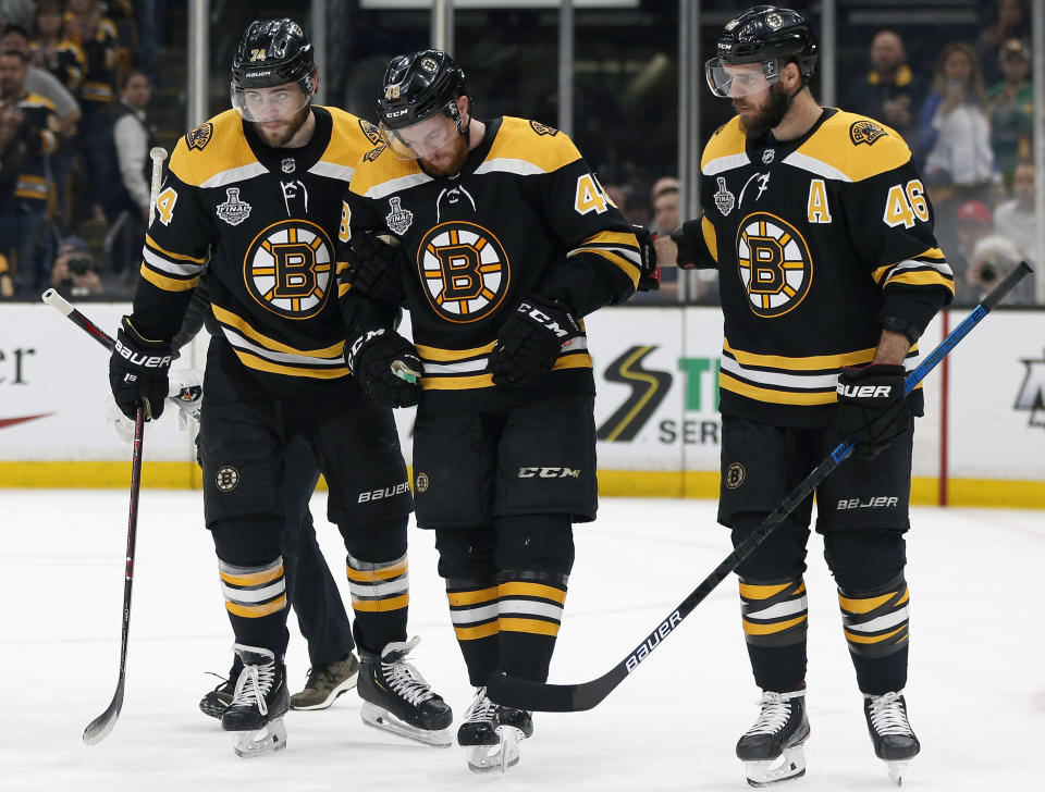 Boston Bruins' Matt Grzelcyk, center, is assisted from the ice by Jake DeBrusk, left, and David Krejci, right, after an injury during the first period in Game 2 of the NHL hockey Stanley Cup Final against the St. Louis Blues, Wednesday, May 29, 2019, in Boston. (AP Photo/Michael Dwyer)