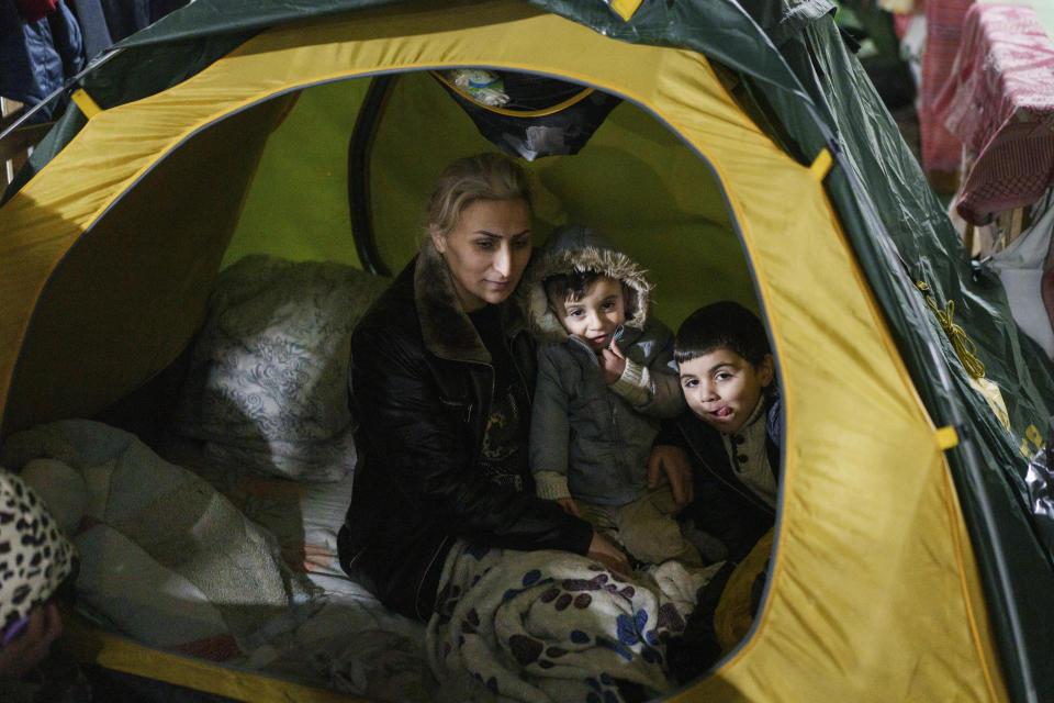 A woman sits with her children inside the tent at the "Bruzgi" checkpoint logistics center at the Belarus-Poland border near Grodno, Belarus, Thursday, Dec. 23, 2021. Since Nov. 8, a large group of migrants, mostly Iraqi Kurds, has been stranded at a border crossing with Poland. Most of them are fleeing conflict or hopelessness at home, and aim to reach Western European countries. But as temperatures fall below freezing, life at the border becomes more challenging. (AP Photo/Pavel Golovkin)