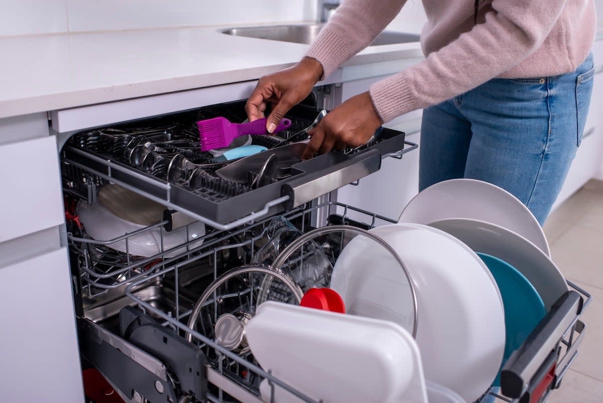 A person loading a dishwasher in their kitchen.