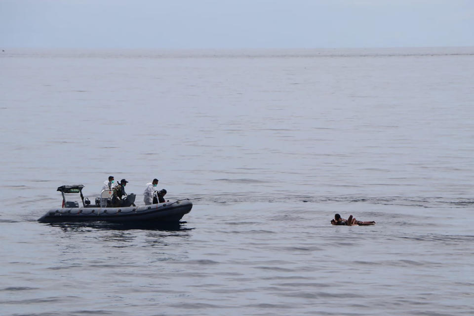 In this photo released by the National Search and Rescue Agency (BASARNAS), rescuers retrieve survivors floating on a wooden plank during a search for victims of a sinking cargo boat in the Makassar Strait, Indonesia, Sunday, May 29, 2022. The search for survivors continue three days after KM Ladang Pertiwi 02 sank in bad weather near Sulawesi Island. (BASARNAS via AP)