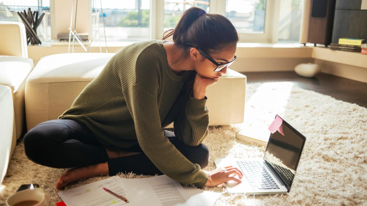 young woman studying and working on her laptop,sitting on the carpet in the living room,nice sunny day.