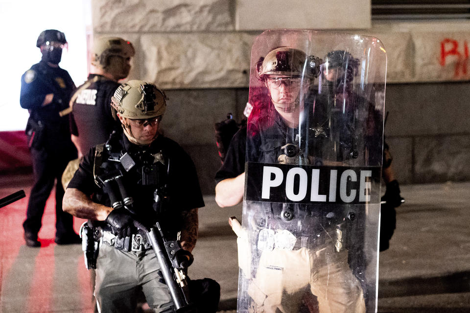 An Oregon State Police officer stands watch as fellow officers extinguish a fire, lit by protesters, behind the Mark O. Hatfield United States Courthouse on Sun, Aug. 2, 2020, in Portland, Ore. Following an agreement between Democratic Gov. Kate Brown and the Trump administration to reduce federal officers in the city, nightly protests remained largely peaceful without major confrontations between protesters and officers. (AP Photo/Noah Berger)