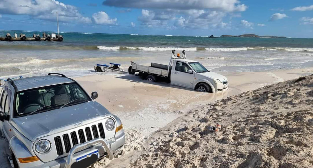 Silver Jeep and white ute bogged on Lancelin Beach in WA during high tide with large swells. 