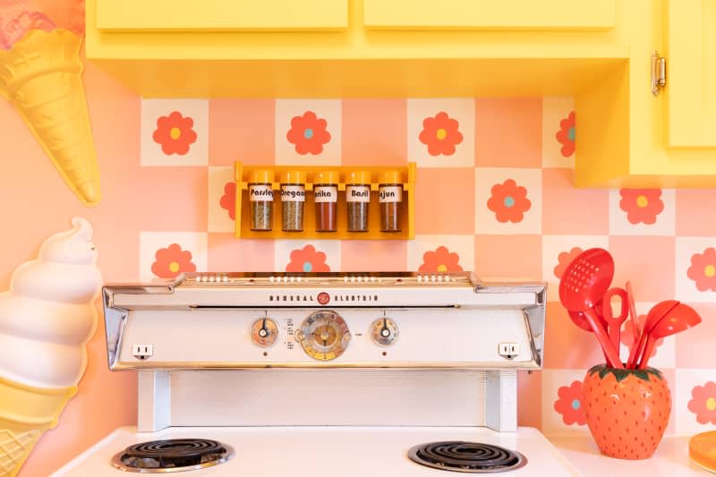 Spice rack mounted above vintage electric stove in kitchen with pink floral motif wallpaper.