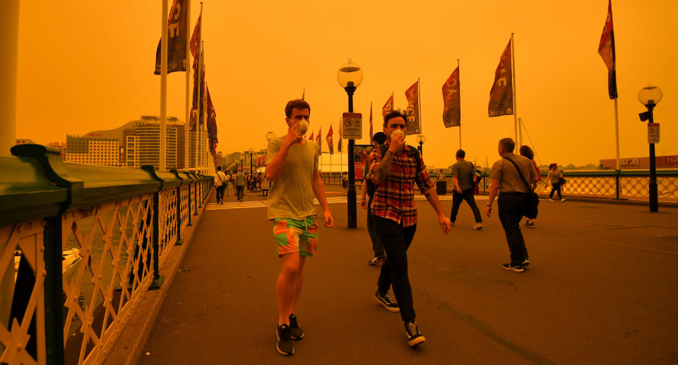 Sydney pedestrians wearing masks walk along a bridge as smoke blankets the city from the NSW bushfires.