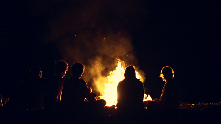 Friends taking part in a moon circle outside at night while sitting near a firepit