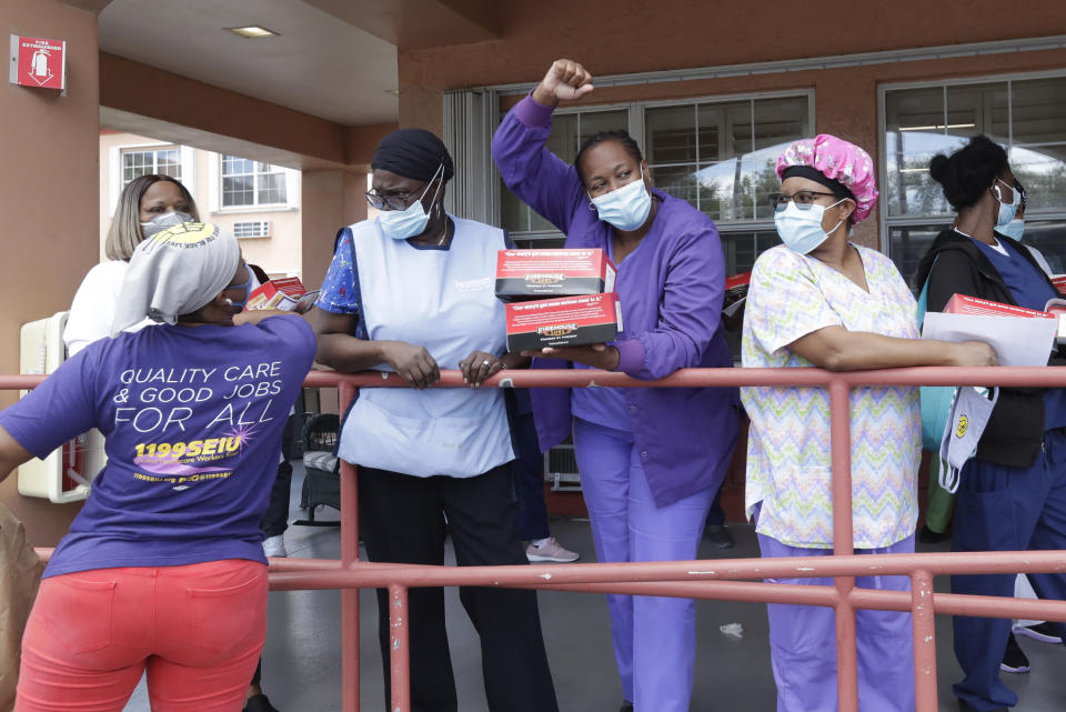Workers at the Franco Nursing & Rehabilitation Center cheer after union members handed out masks to prevent the spread of the new coronavirus and lunches, Monday, July 20, 2020, in Miami. Most facilities, experts and industry leaders told The Associated Press that a statewide mask mandate would help protect staff members, and consequently residents, from the virus. (AP Photo/Wilfredo Lee)